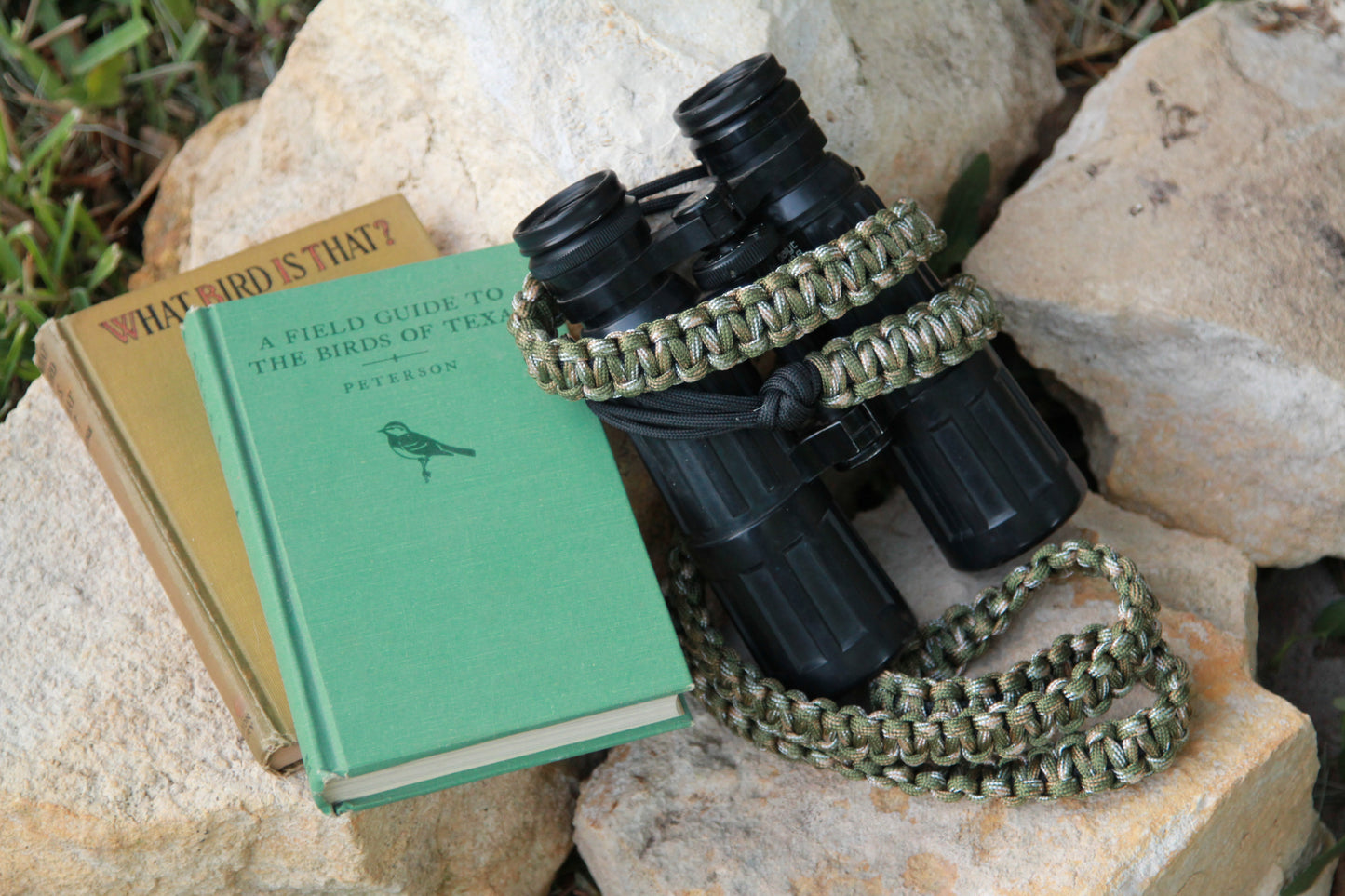 This photo shows a paracord Venture Strap attached to a pair of antique binoclulars beside to older bird field guide books. The Venture Strap is a binocular or camera strap made of sturdy paracord. The strap is worn across the body and is more comfortable and durable that traditional binocular harnesses or camera straps. 